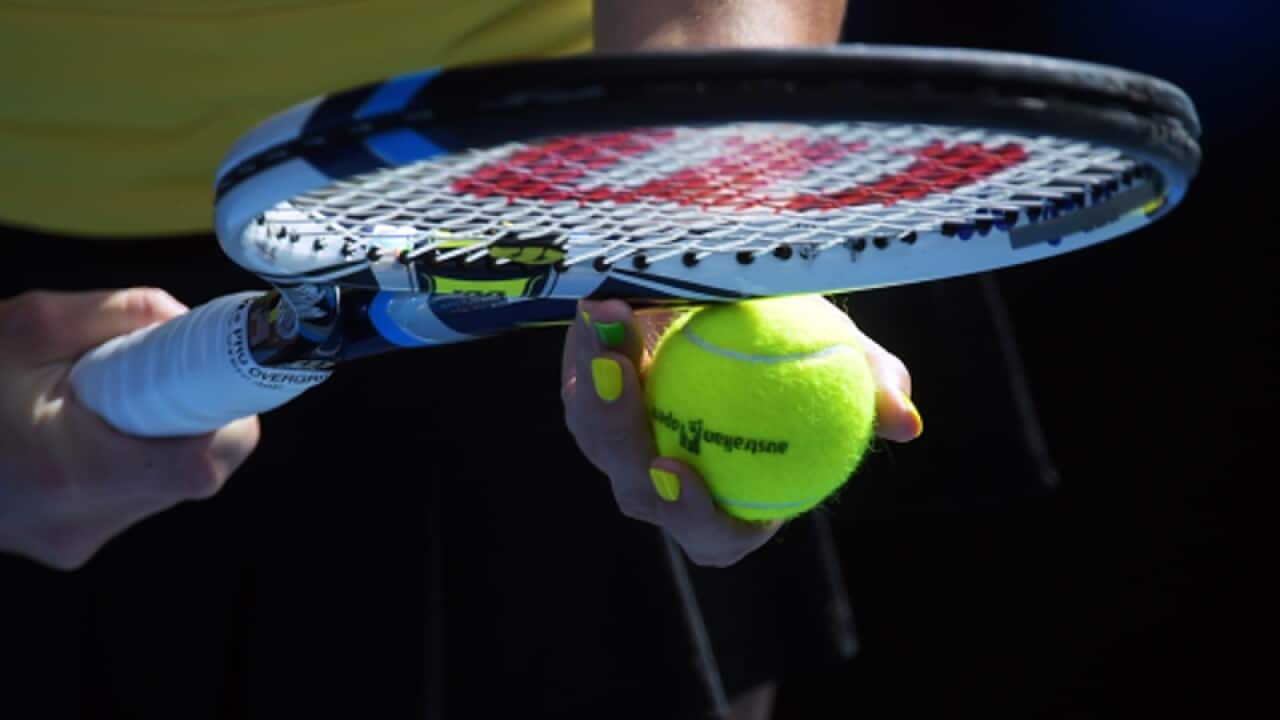 A tennis player holds a racquet and balls