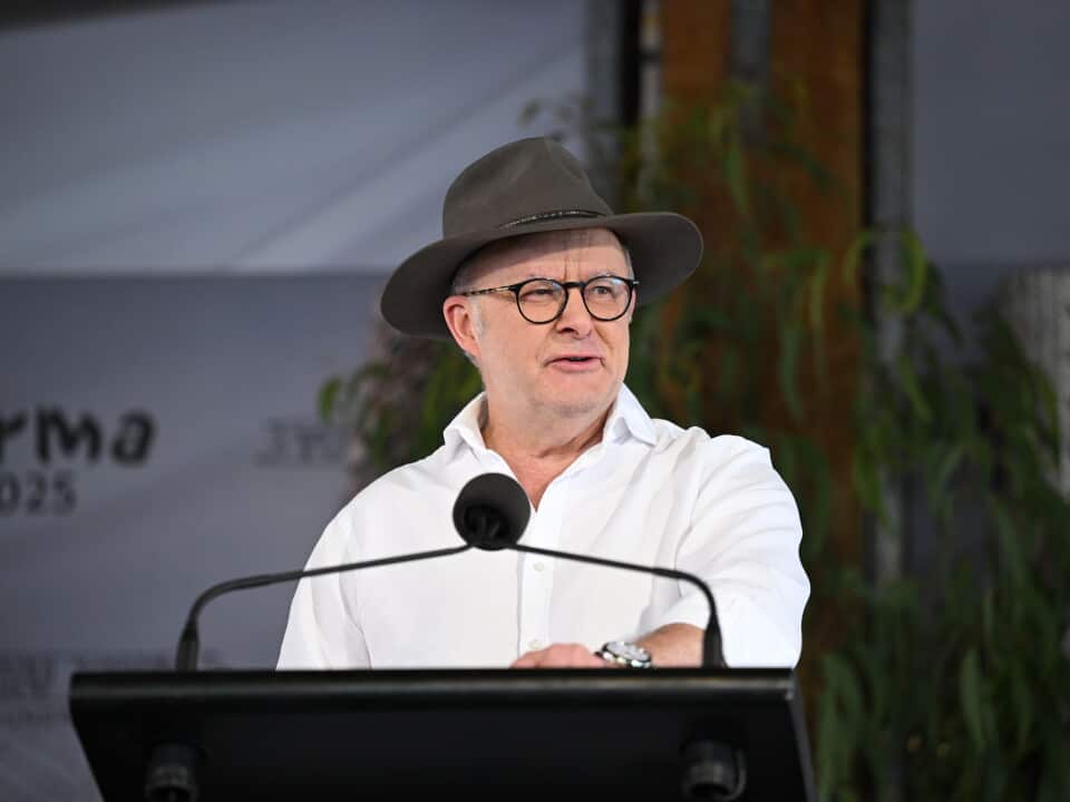A man wearing a white shirt and hat speaks at a podium.
