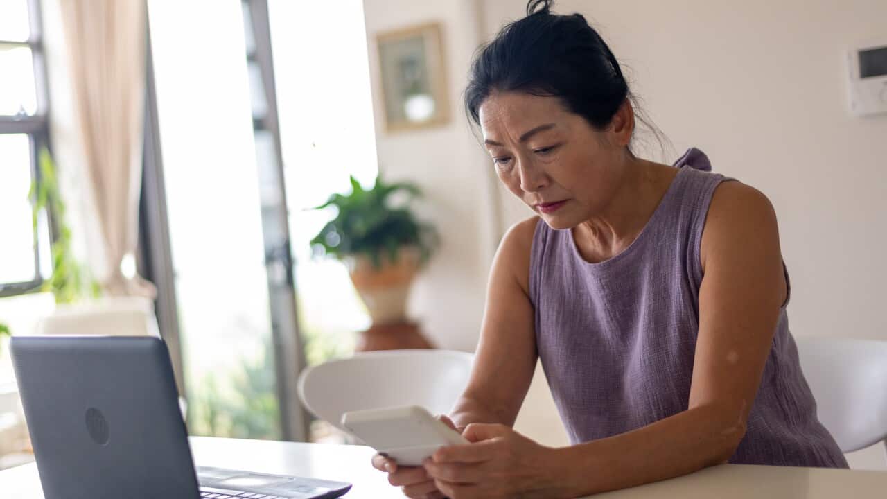 A woman looking stressed with a calculator, laptop and bills sits at a table inside
