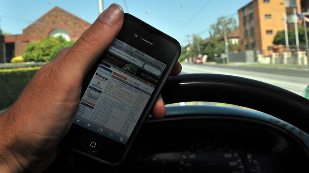A driver holds a mobile phone whilst driving in Melbourne