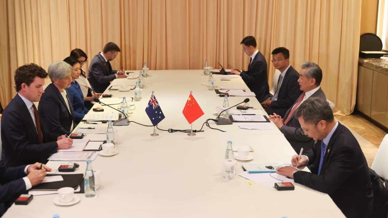 An Australianflag and a Chinese flag sit in the centre of a table, flanked by diplomats