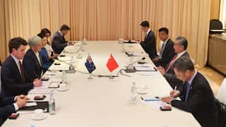 An Australianflag and a Chinese flag sit in the centre of a table, flanked by diplomats