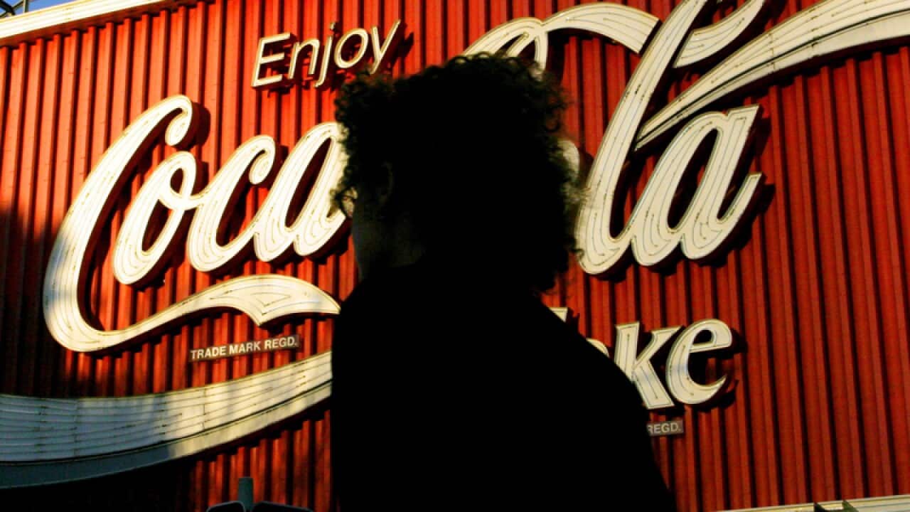 a woman walking past a large sign advertising Coca Cola