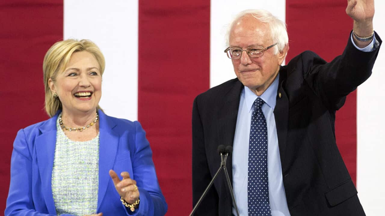Hillary Clinton smiles as she arrives on stage with Bernie Sanders