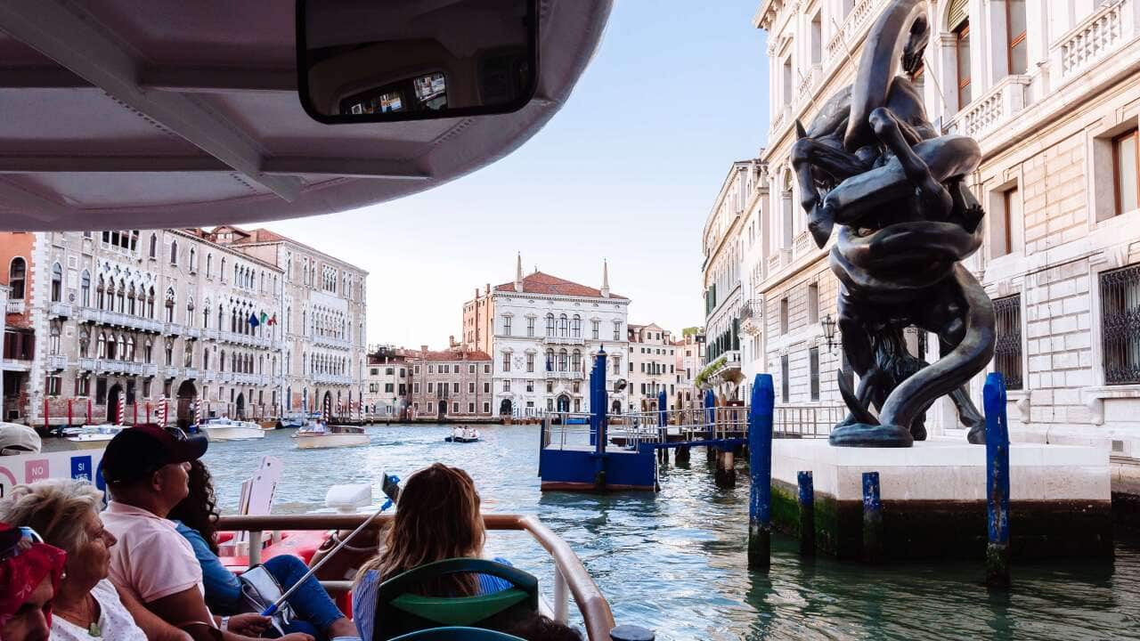 Tourists in a vaporetto looking at a sculpture.