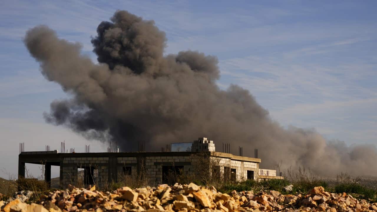 Black smoke rises from a building surrounded by rocks.