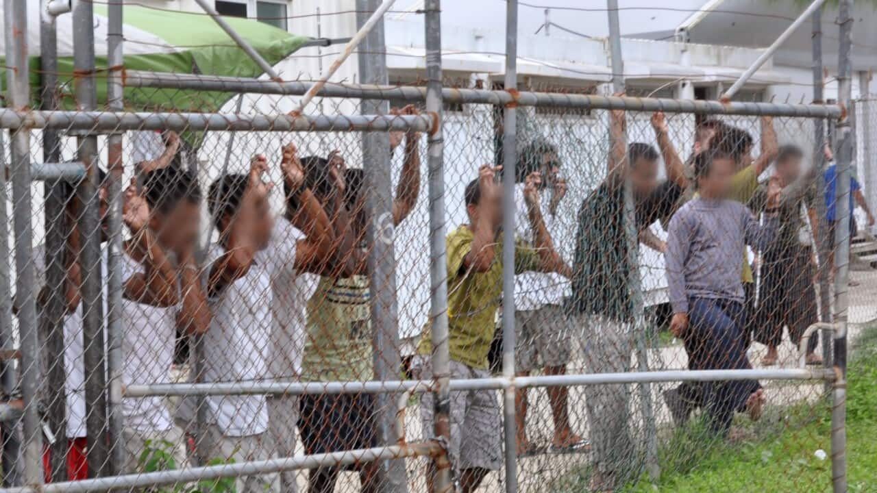 People line up at a chain link fence at a detention centre on Manus Island. Their faces are blurred.