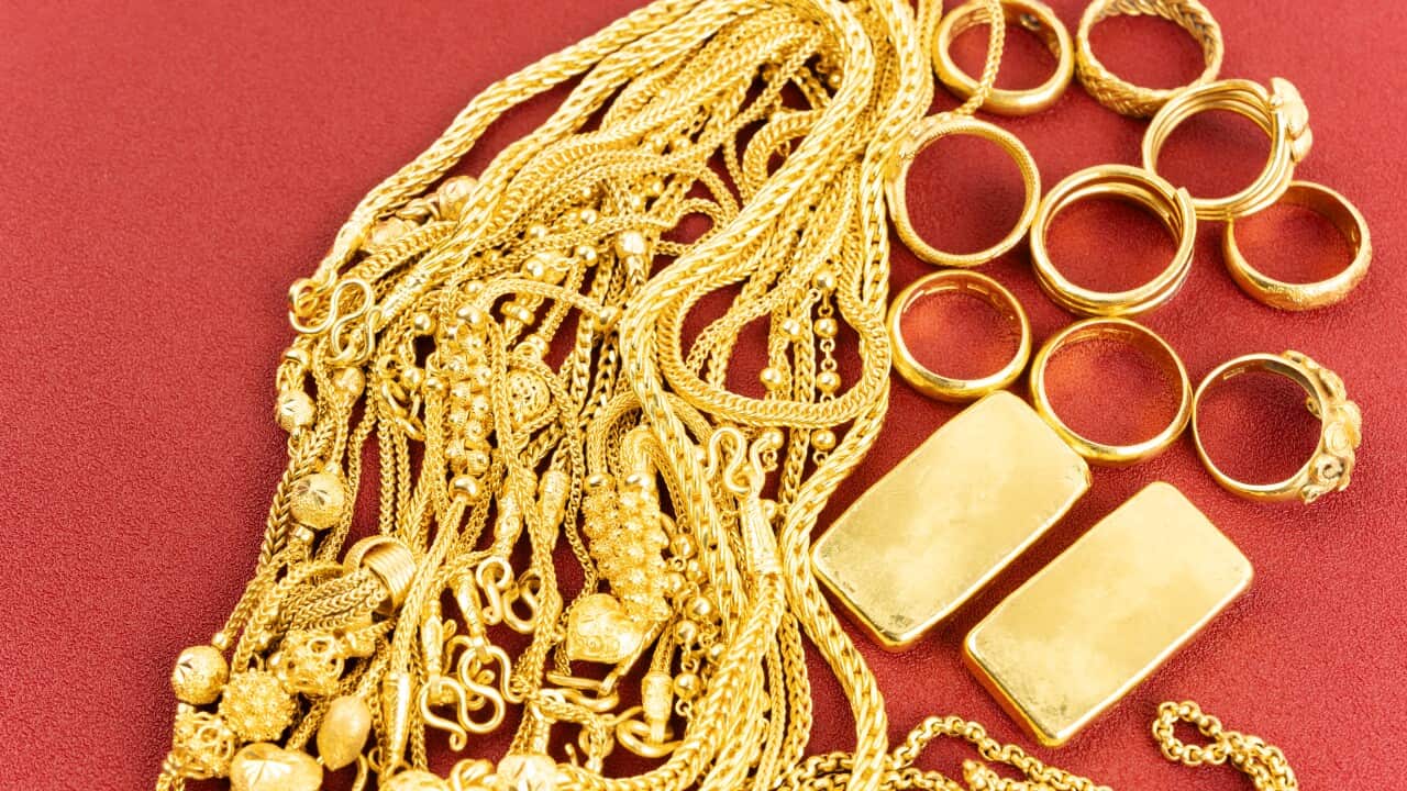 Group of gold necklaces, rings and gold bars on red leather background