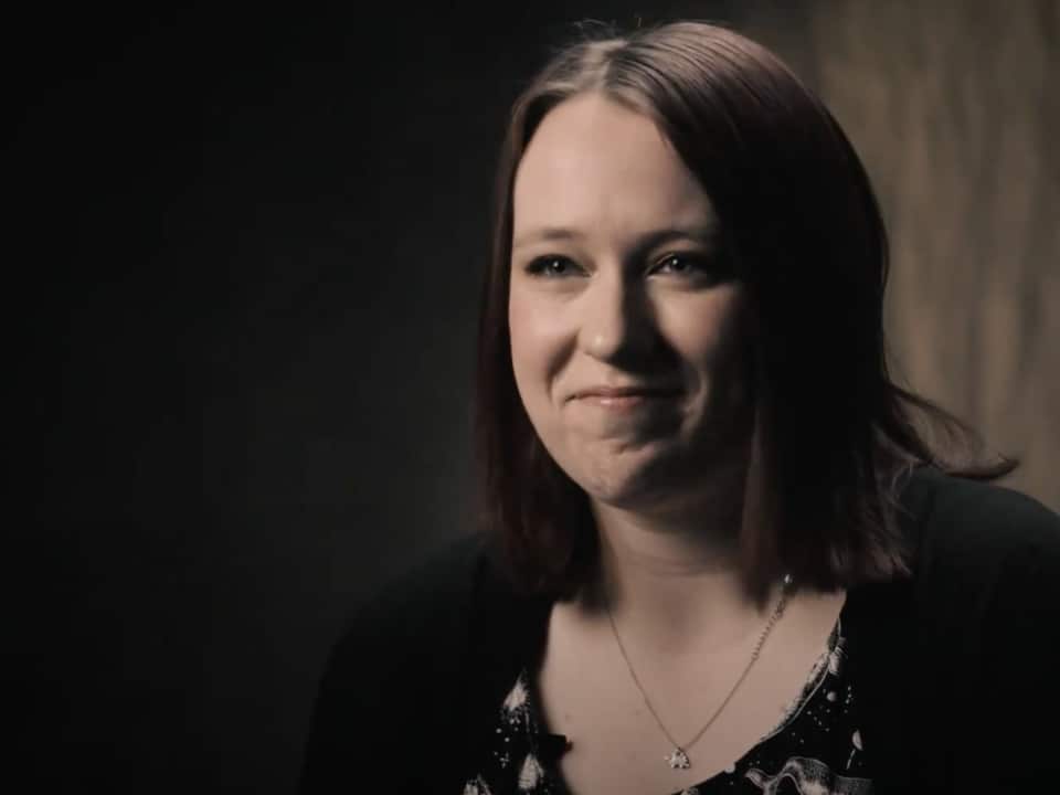A woman with short hair in a black cardigan smiles at the camera.