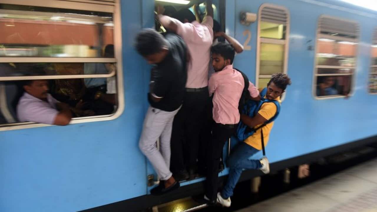 Sri Lankan passengers hold on to door handles as they travel in a full carriage of a train during a nationwide railway strike