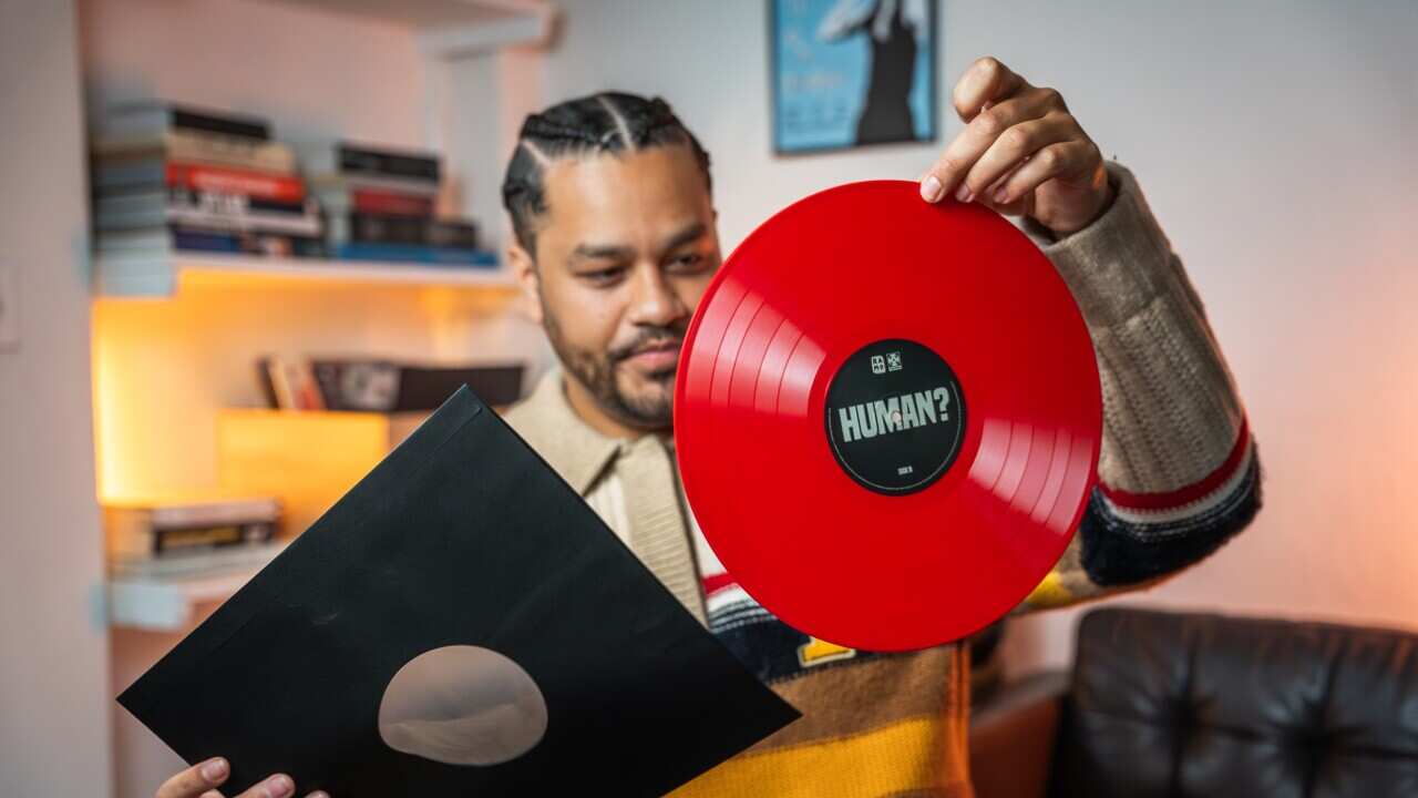 A man in a jumper holds up a red record after removing it from the sleeve.