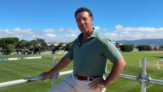 A man in a green tee standing in front of a pitch with a smile