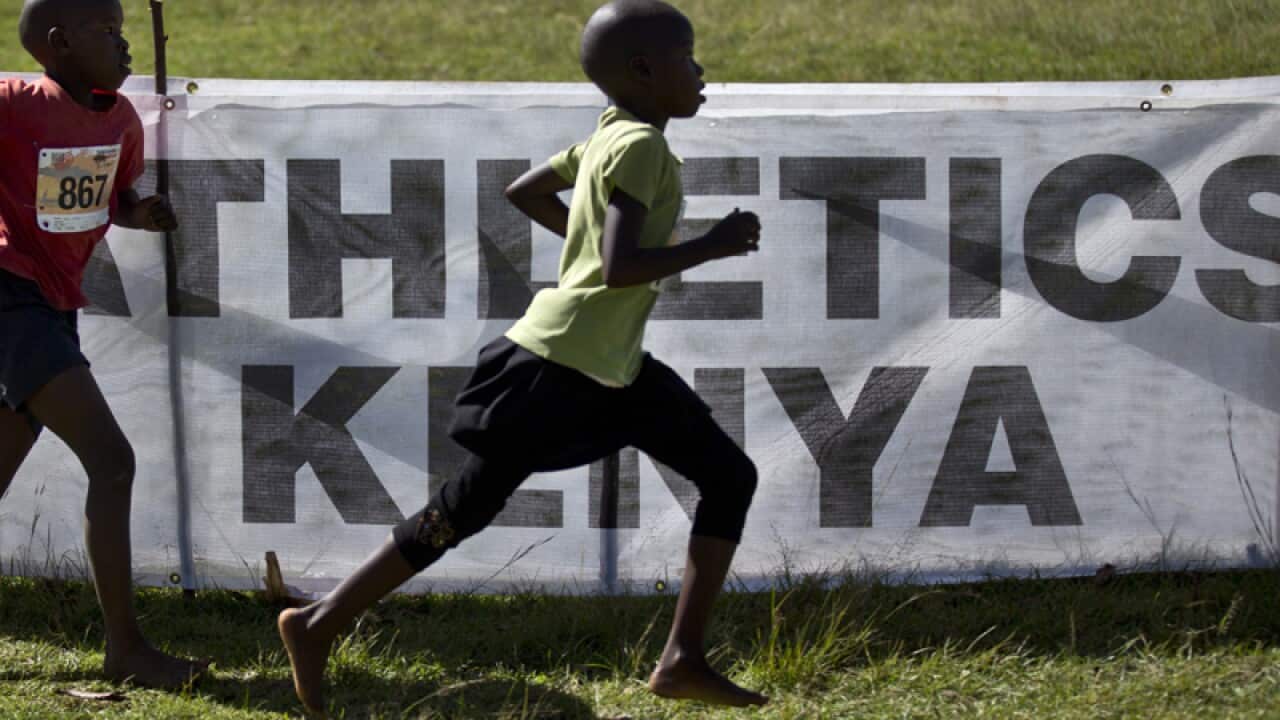 junior athletes run past a sign for Athletics Kenya.