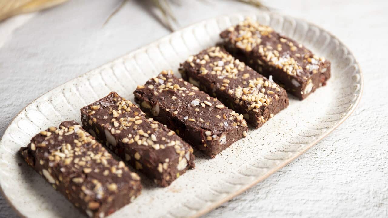 Five pices of rocky road, sprinkled with crushed peanuts, sit on a pale oval platter with decoratively marked edges.