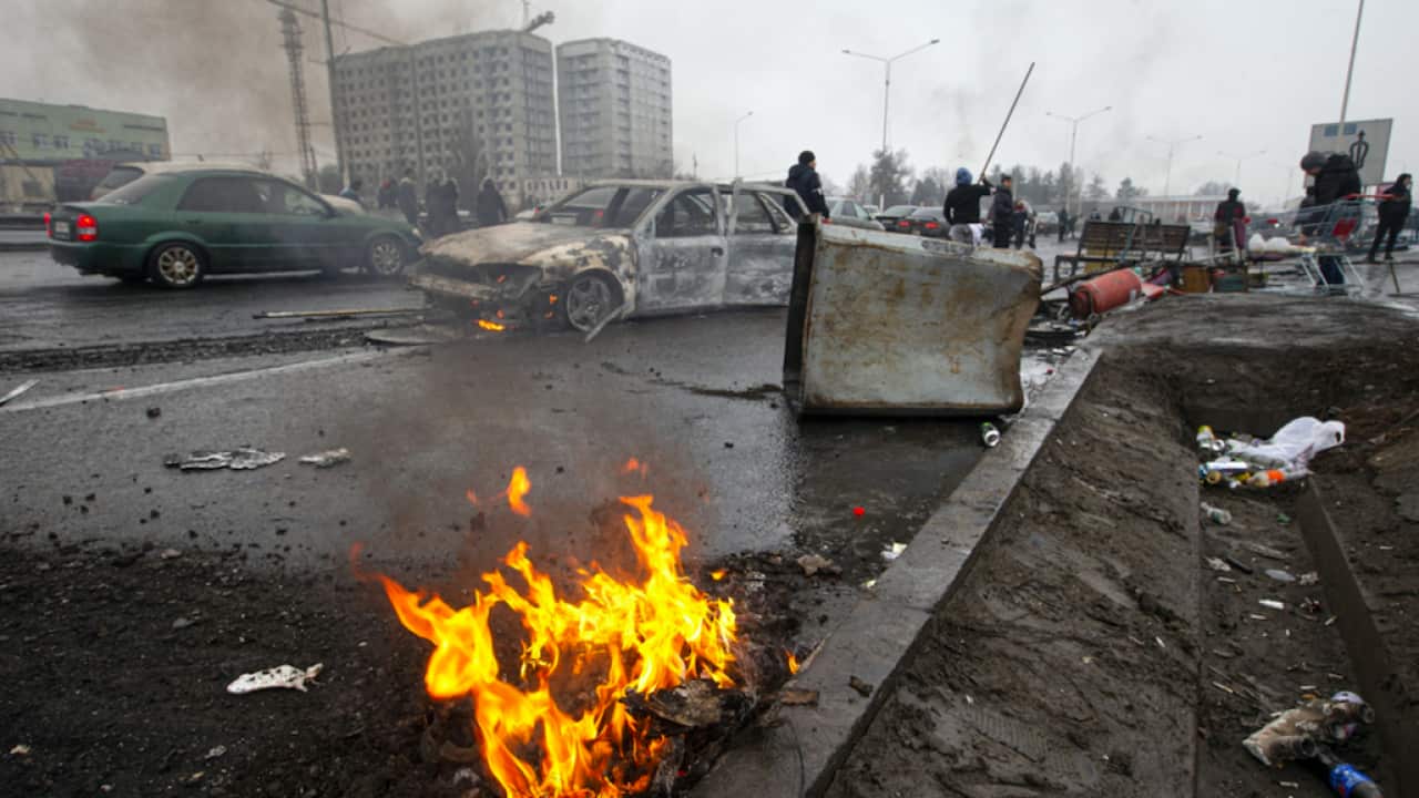 People walk past cars, which were burned after clashes, on a street in Almaty, Kazakhstan, 7 January, 2022.