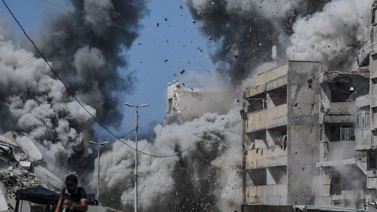A man flees from an airstrike that sends dense plumes of dark smoke and debris flying from heavily damaged buildings.