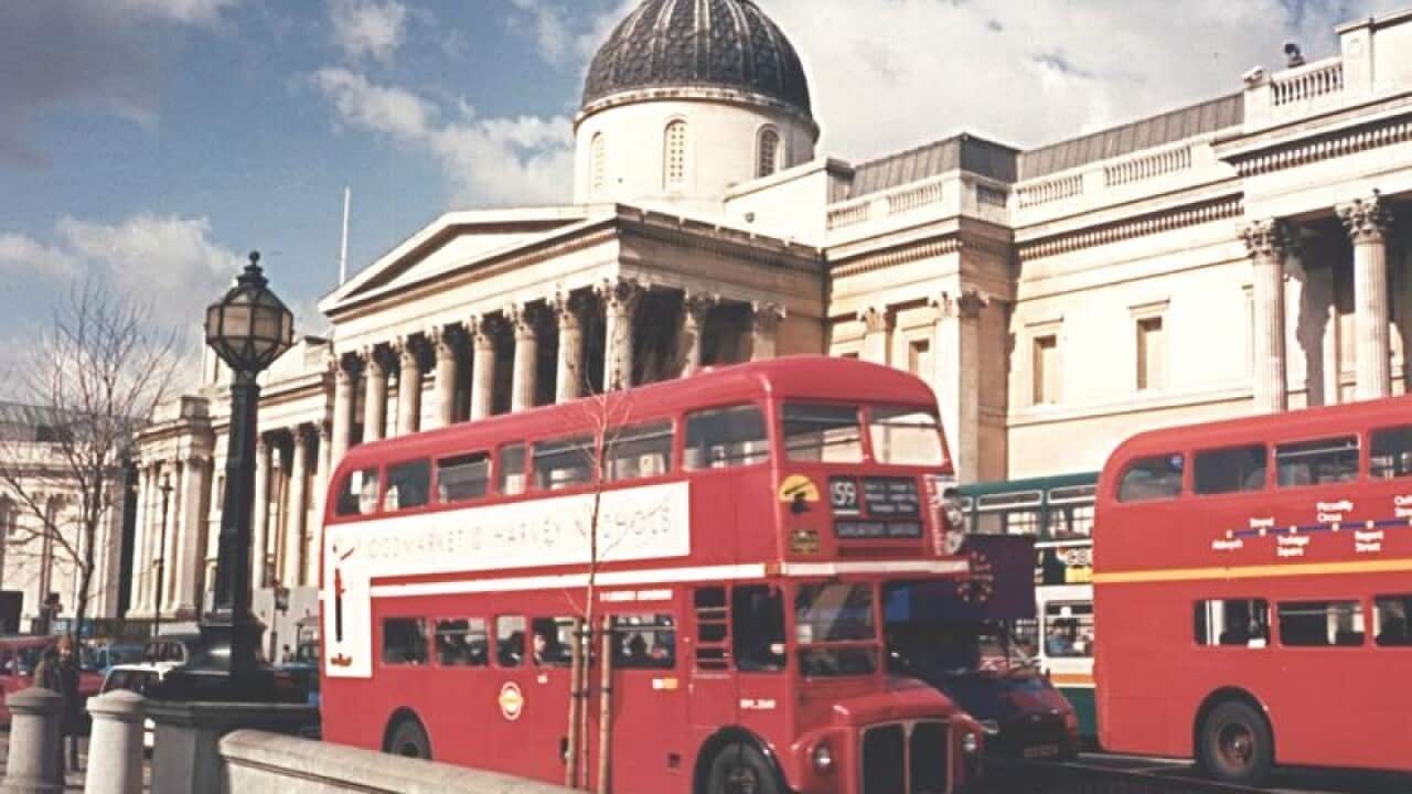Red double decker buses pass by The National Gallery in London