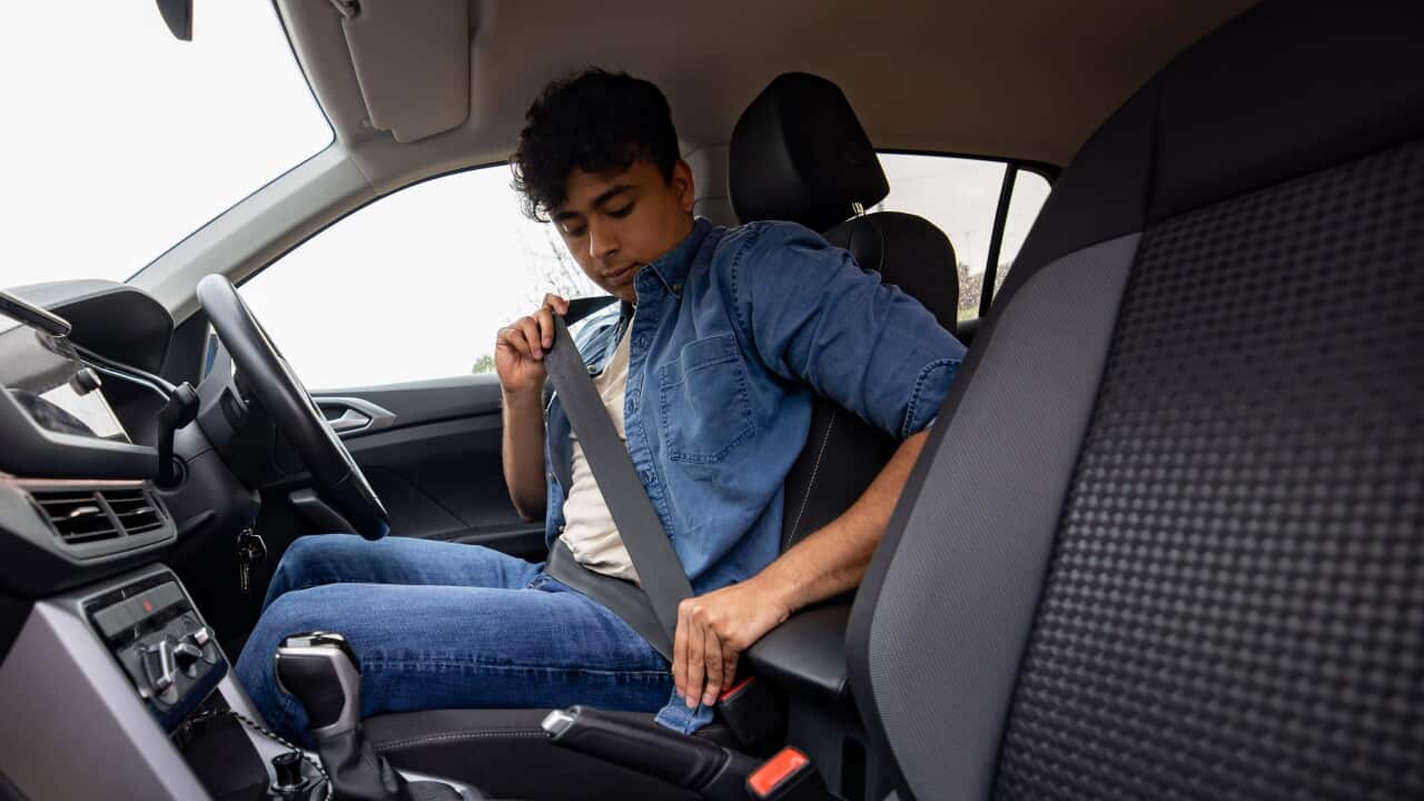 A young man putting on his seatbelt in a right hand side drive car.