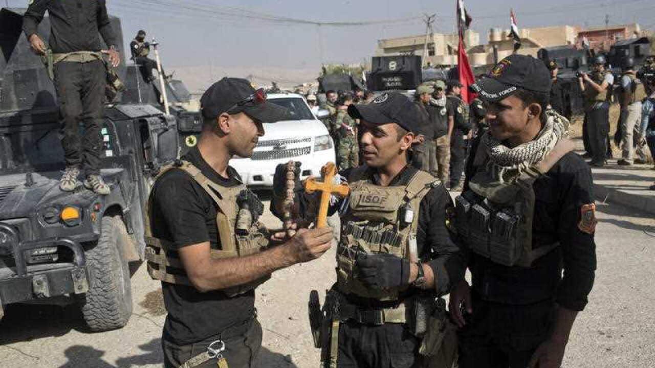 Iraqi Special Forces soldiers hold a cross found in the town of Bartella, Iraq