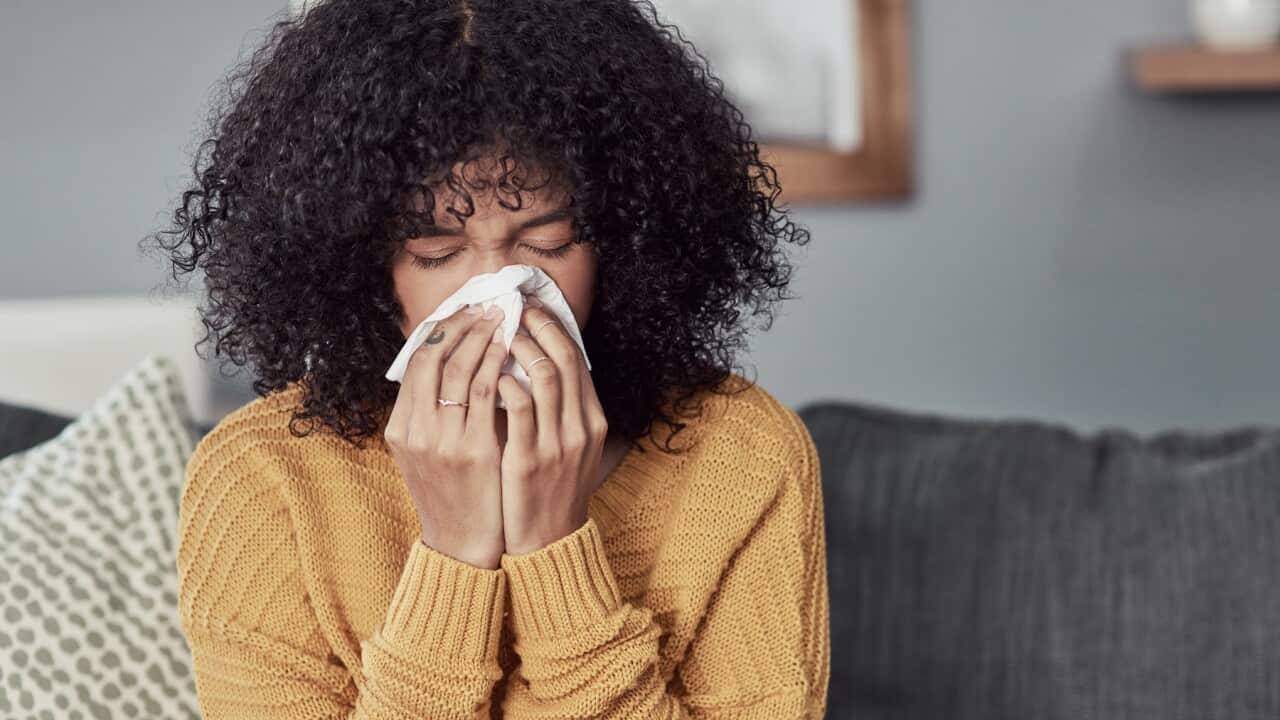 Shot of a young woman blowing her nose at home