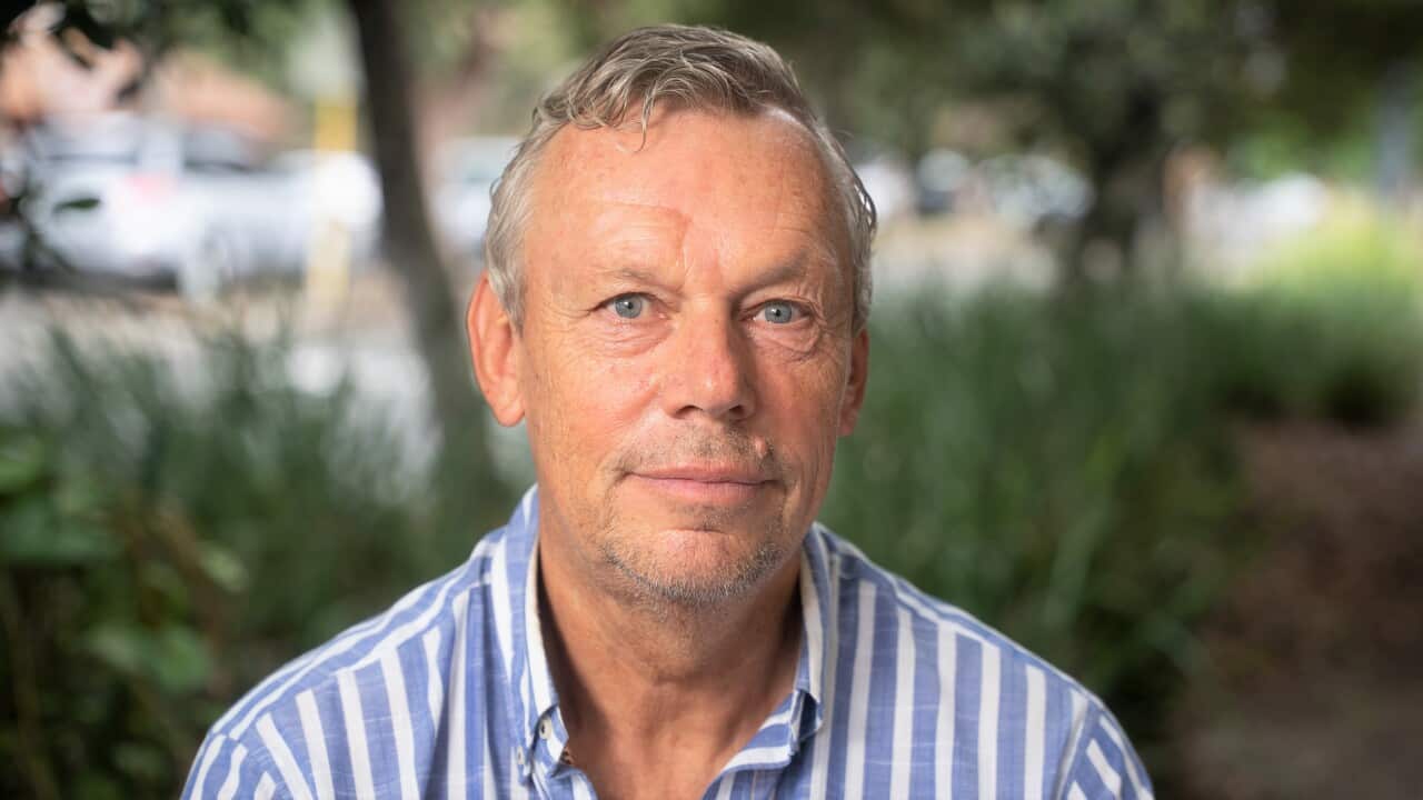 A man wearing a blue-and-white striped shirt and sitting in a garden.