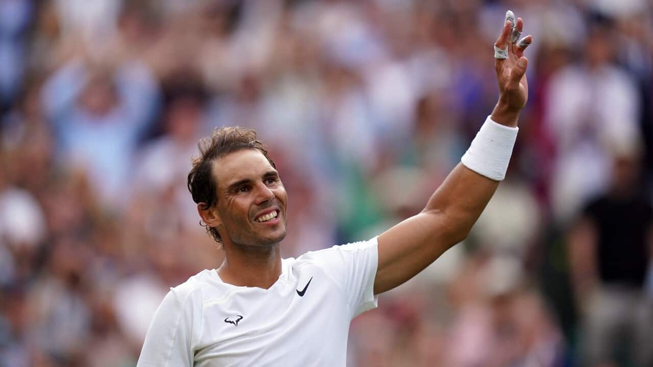 A man in a white uniform waves on a tennis court