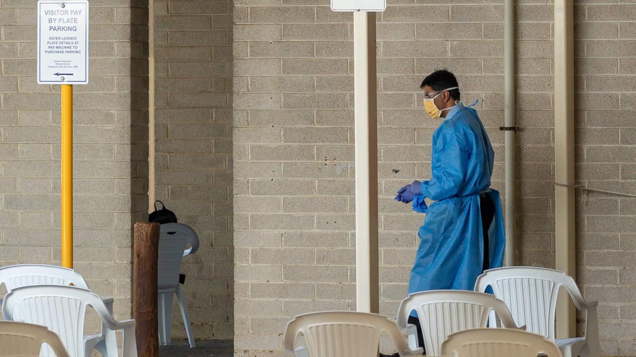 A person in hospital scrubs walks through a Covid testing centre lined with empty white chairs.