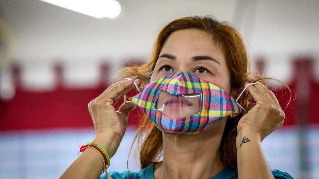 An employee with hearing impairment puts a see-through face mask designed for people who are deaf or hard of hearing