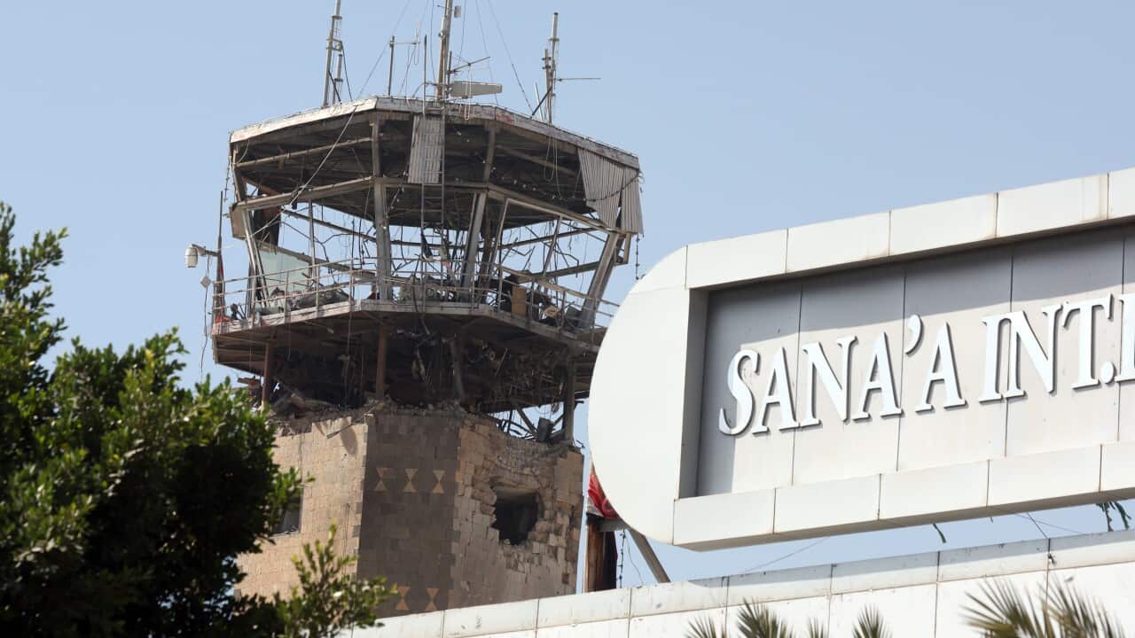 A destroyed airport control tower next to a sign on a brick building that says 'Sana'a'