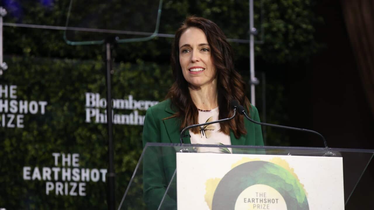 Jacinda Ardern wearing a green jacket standing behind a lectern.
