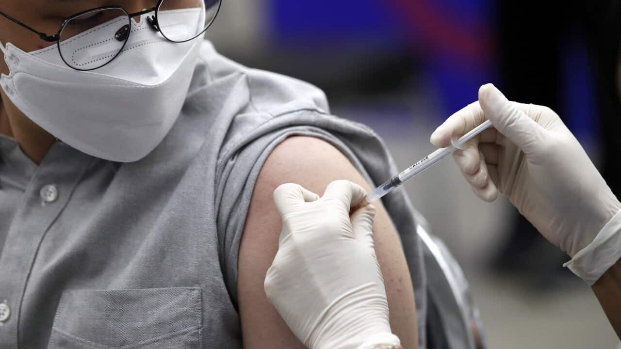 A person wearing a mask being injected in the arm with a syringe.
