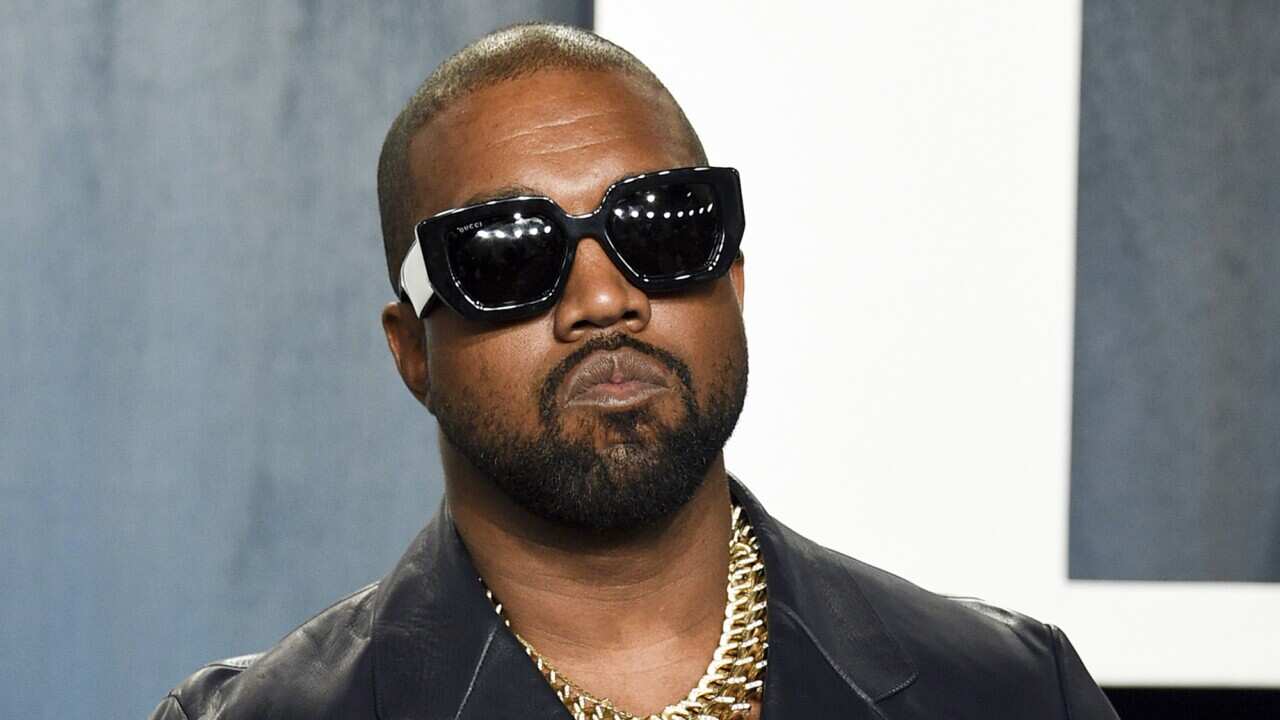 Kanye West wearing dark sunglasses, a dark shirt and a gold chain