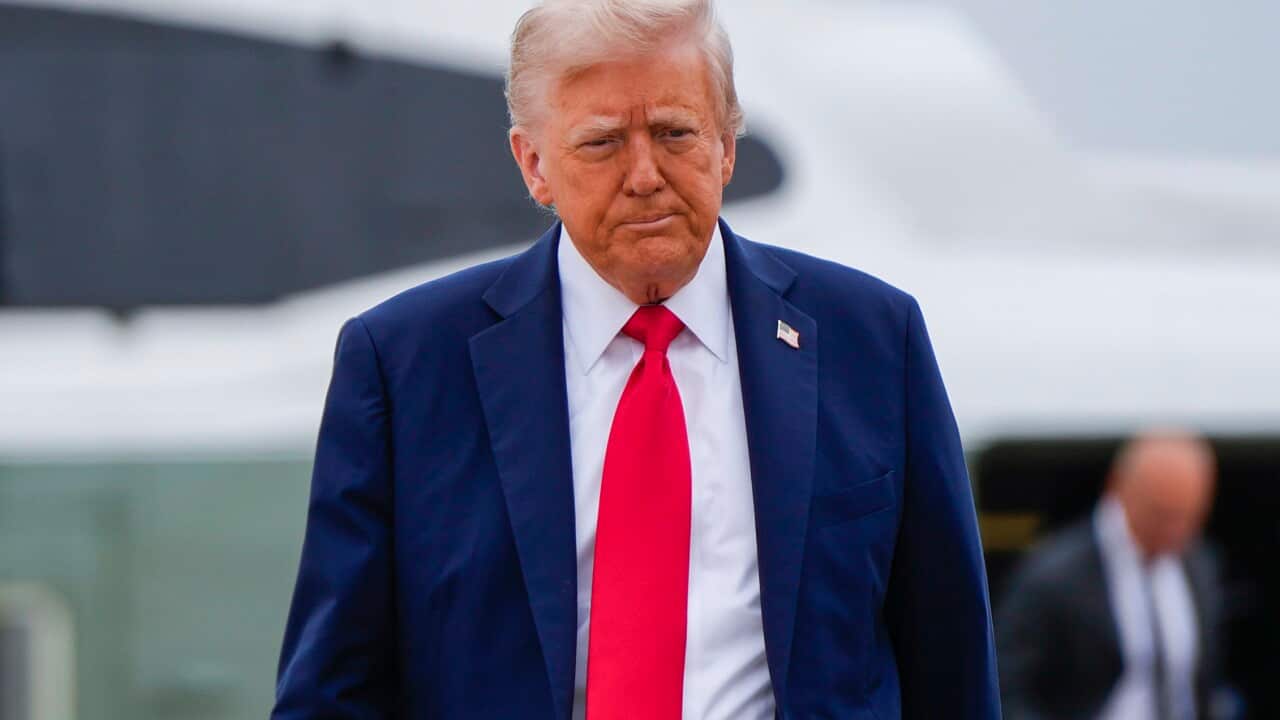 Donald Trump, wearing a blue suit with an American flag pin on it, white shirt and red tie.