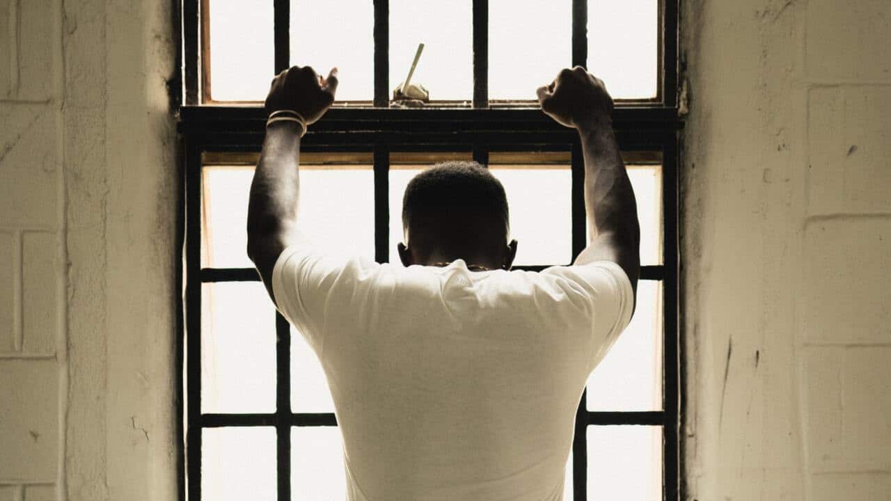 Umugabo yambaye umupira wera n'ipantalo yirabura yishimikije idirisha.