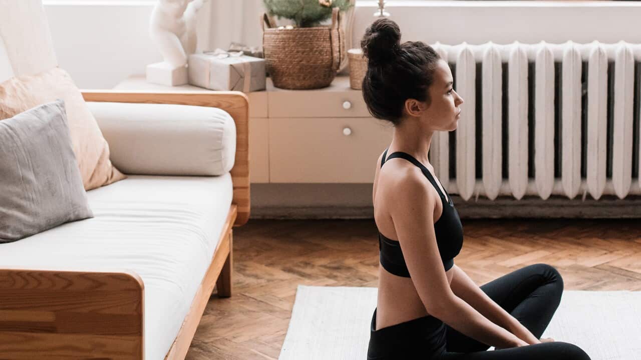Woman sitting cross-legged in living room, preparing for meditation
