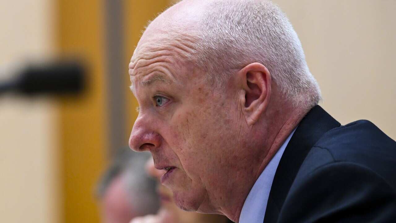 A balding man in a suits peaks into a microphone