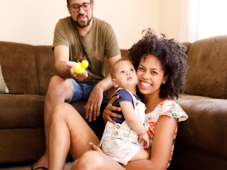 Father, baby and mother playing on the sofa at home.