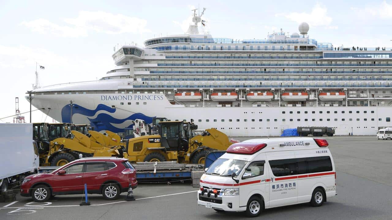 An ambulance leaves Yokohama Port on Feb. 18, 2020, with the Diamond Princess cruise ship seen in the background. The ship has been kept in quarantine amid the spread of a new coronavirus among people on board. (Kyodo via AP Images) ==Kyodo