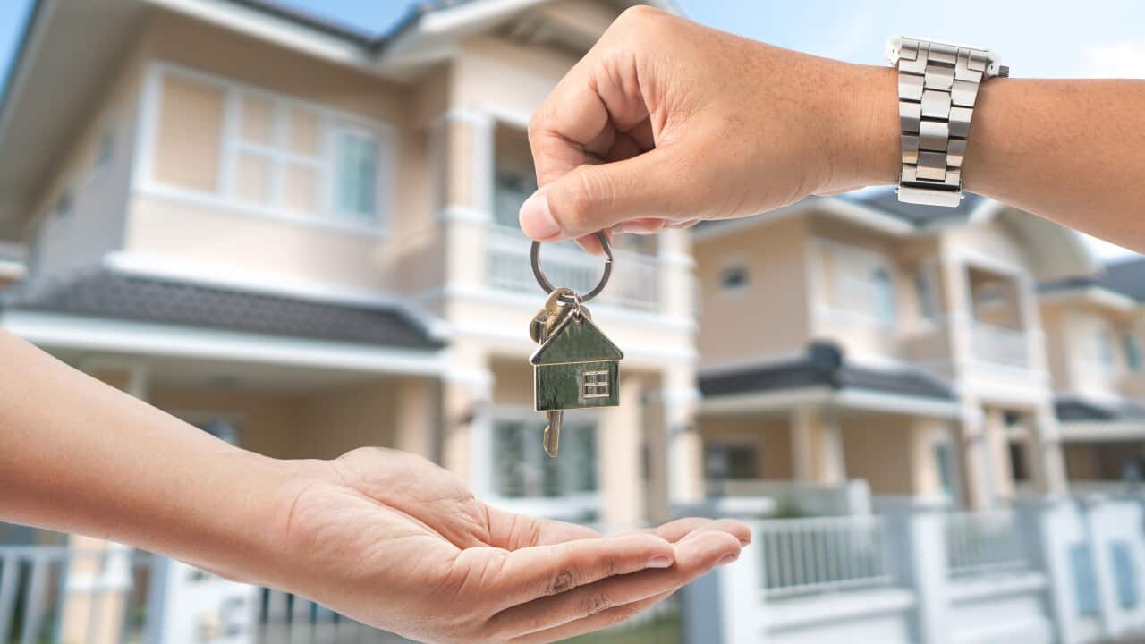 Man is handing a house key to a woman.Key with a keychain in the shape of the house.