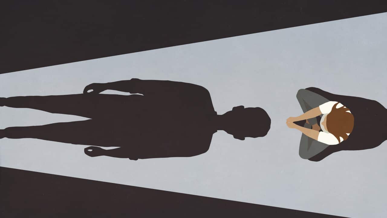 Woman sitting before looming male shadow