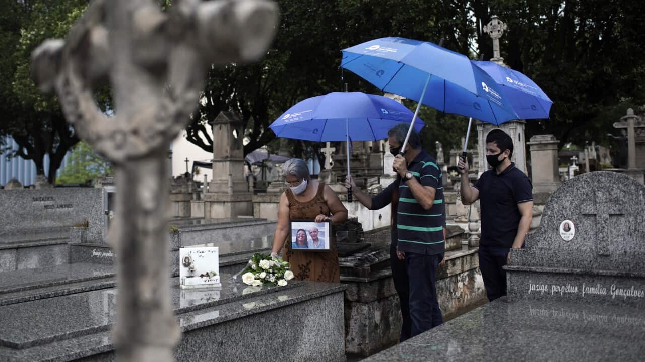 Giselle Peixoto holds a portrait of herself with her late father Geraldo Diniz, who died from COVID-19, as she places flowers on his tomb at the Penitencia cemetery in Rio de Janeiro, where a memorial will honour his name and thousands of others.