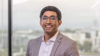 a close up of a young man in a suit and glasses smiling in a glass office