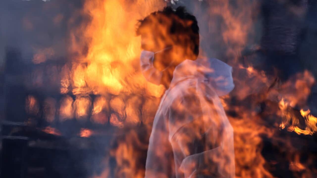 A municipal worker wearing personal protective equipment (PPE) is seen through funeral pyres for COVID-19 victims at a cremation ground in Mumbai