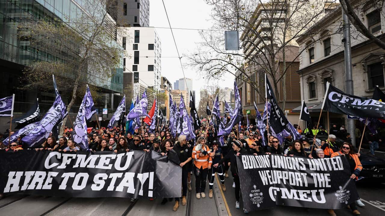 A large group of protesters holding CFMEU signs and marching down the street.