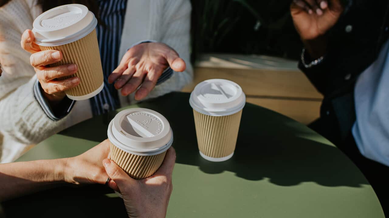A group of colleagues sit at a table outdoors and enjoy some takeaway coffees