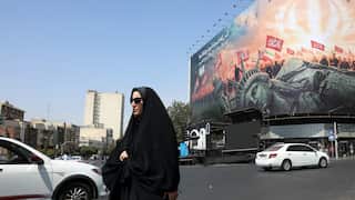 A woman dressed in black walking in front of a billboard showing a toppled Statue of Liberty.
