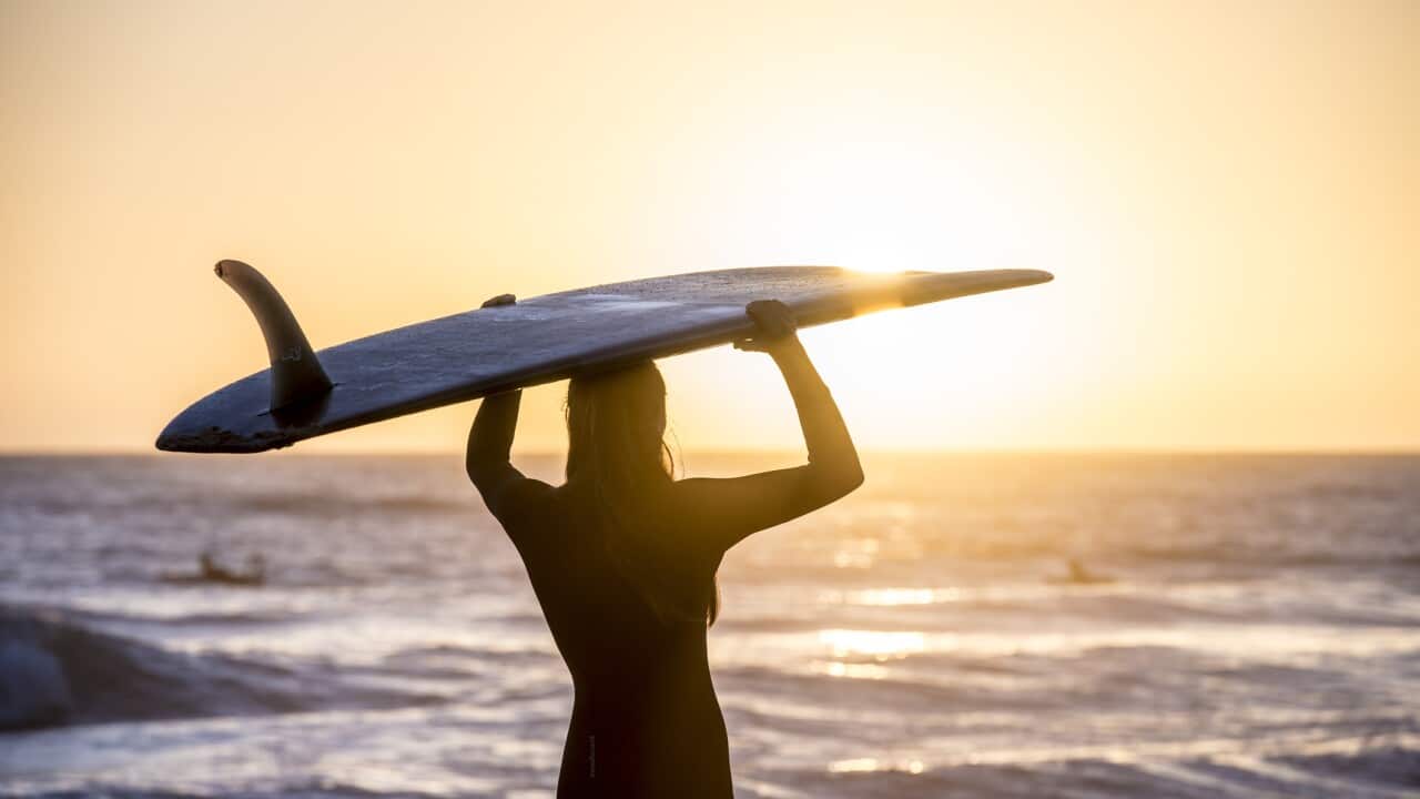 female surfer at sunrise standing on beach