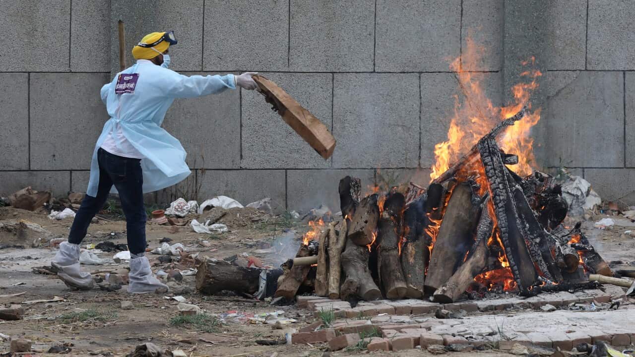 An Indian volunteer is seen near burning pyre during a mass funeral of COVID-19 victims in New Delhi.