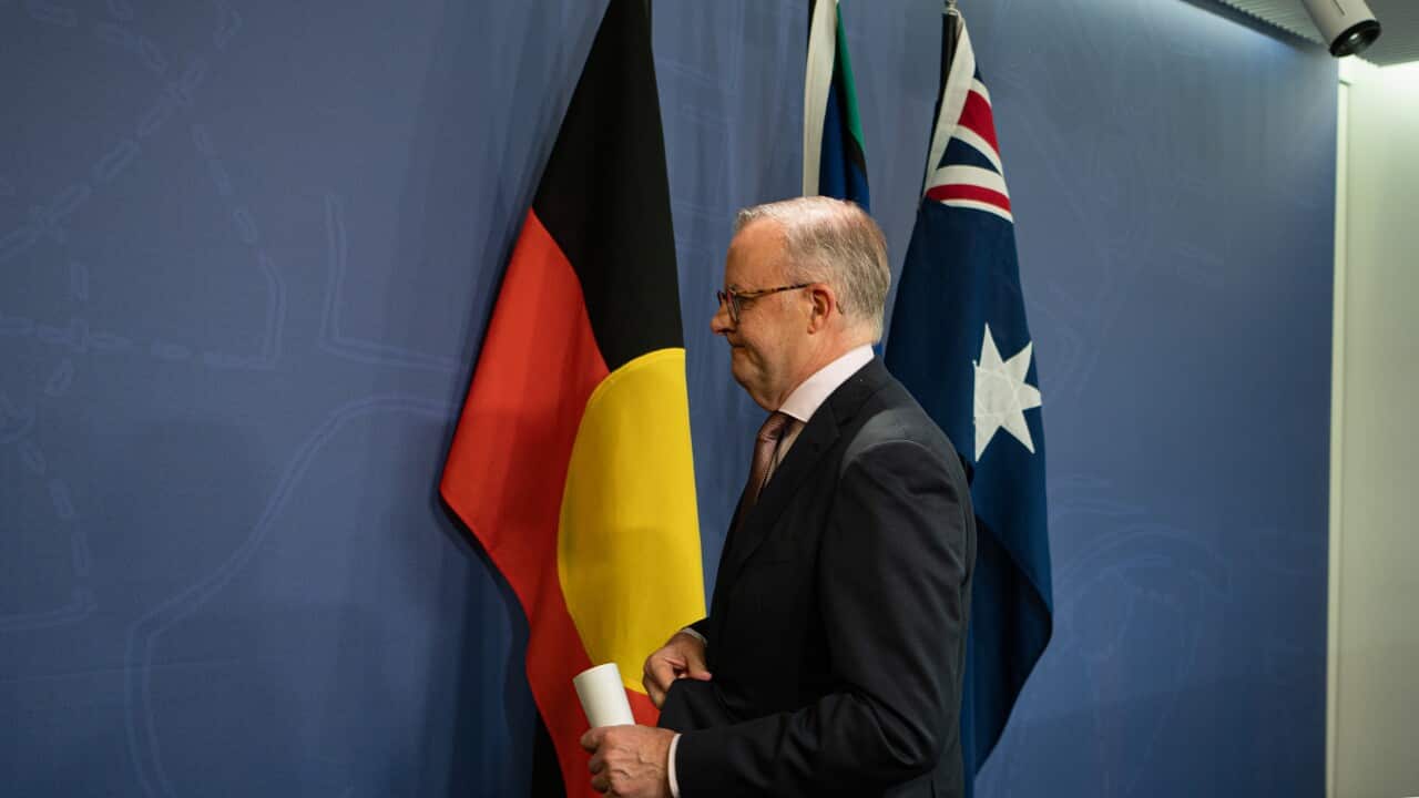 Anthony Albanese leaves a press conference in front of three flags.