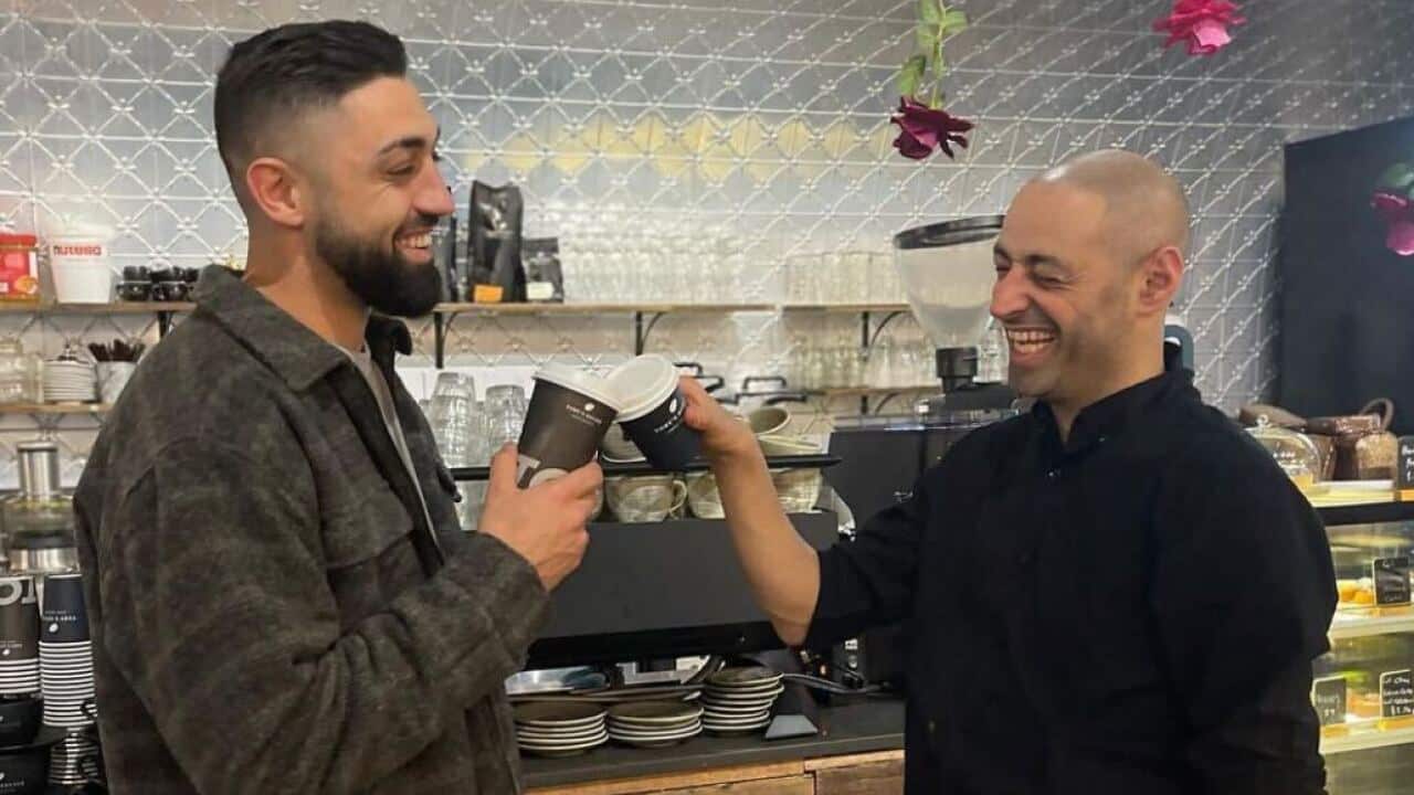 Two men clink coffee cups together.